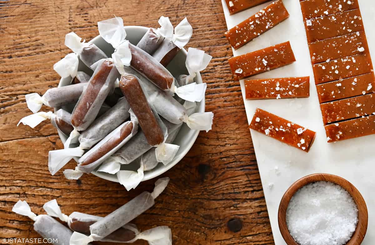 Soft homemade caramels wrapped in wax paper next to more that haven't been wrapped yet.