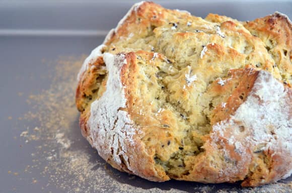 A loaf of homemade Irish soda bread sits on a flour-dusted surface