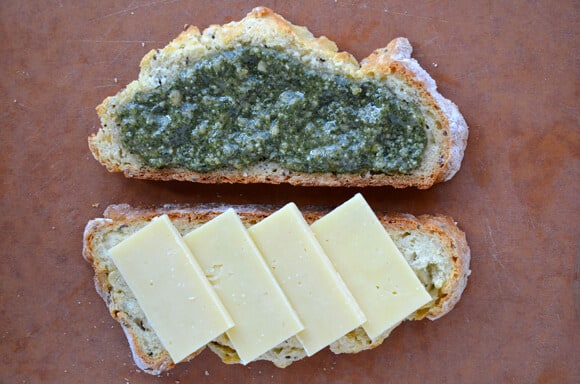 A slice of of homemade Irish soda bread is slathered with pesto and another slice is stacked with cheddar cheese.