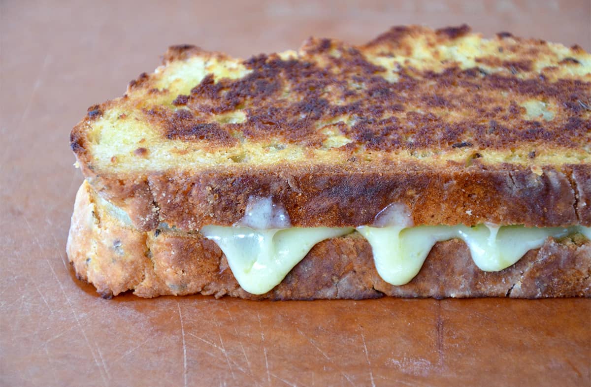 Gooey melted cheese oozy out from a grilled cheese sandwich.