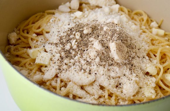 Green pot with cooked spaghetti topped with grated Parmesan and black pepper 