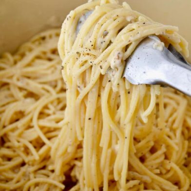 A green pot containing Cacio e Pepe Pasta and tongs