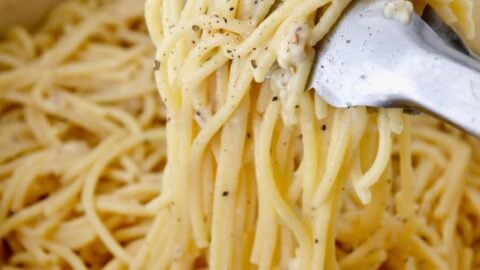 A green pot containing Cacio e Pepe Pasta and tongs
