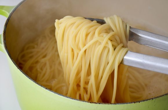 Green pot with cooked spaghetti and tongs