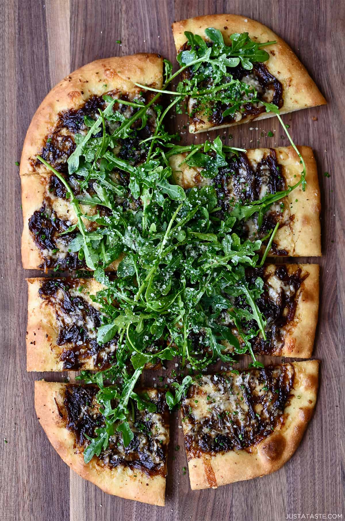 Pizza with caramelized onions, melted gruyere cheese and fresh arugula sliced into rectangles.