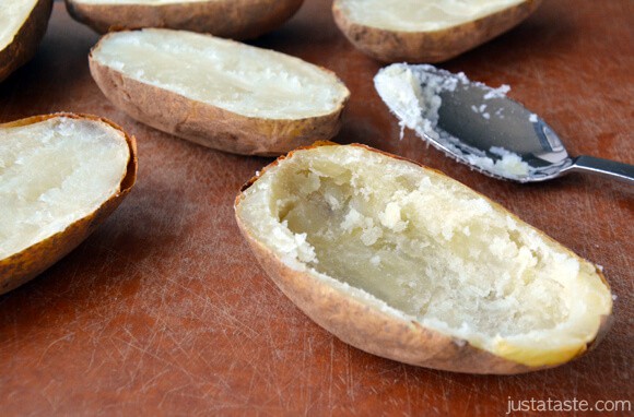 A baked potato with its interior scooped out and a spoon sitting beside it. More baked potatoes are off to the side.