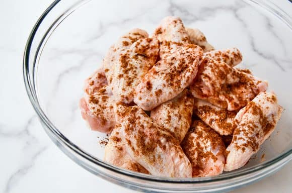 Clear bowl containing unbaked chicken wings with seasoning 