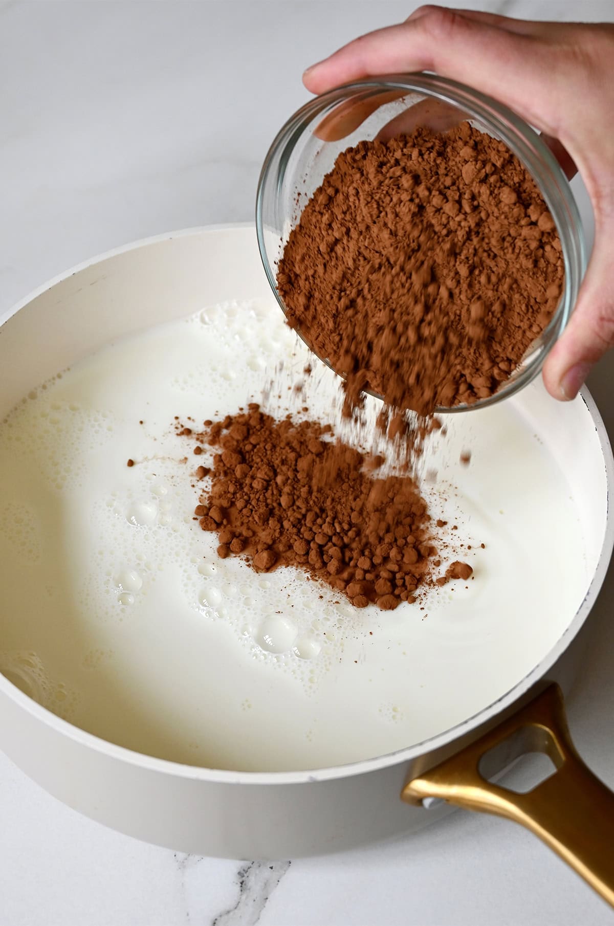 Adding cocoa powder to a saucepan with whole milk.