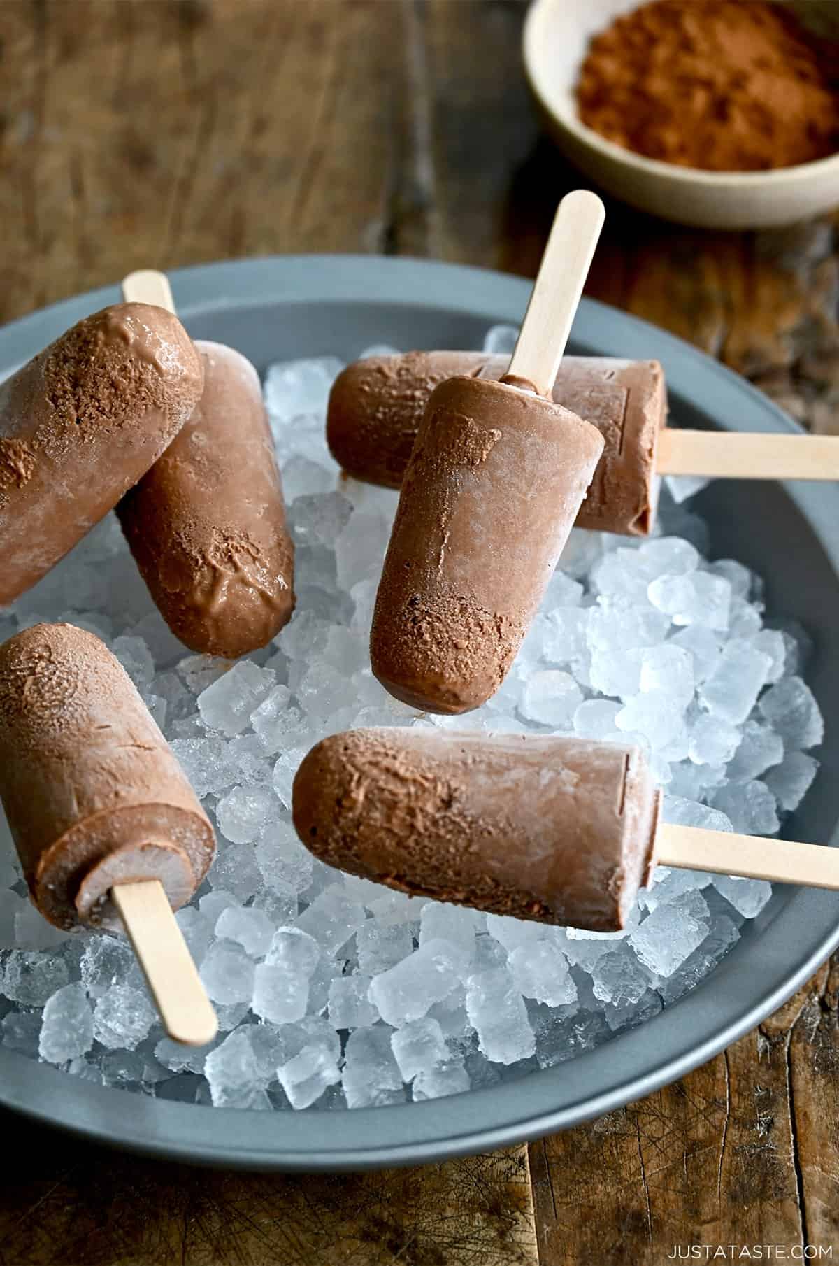 Homemade fudge pops with wooden popsicle sticks on a bed of ice.