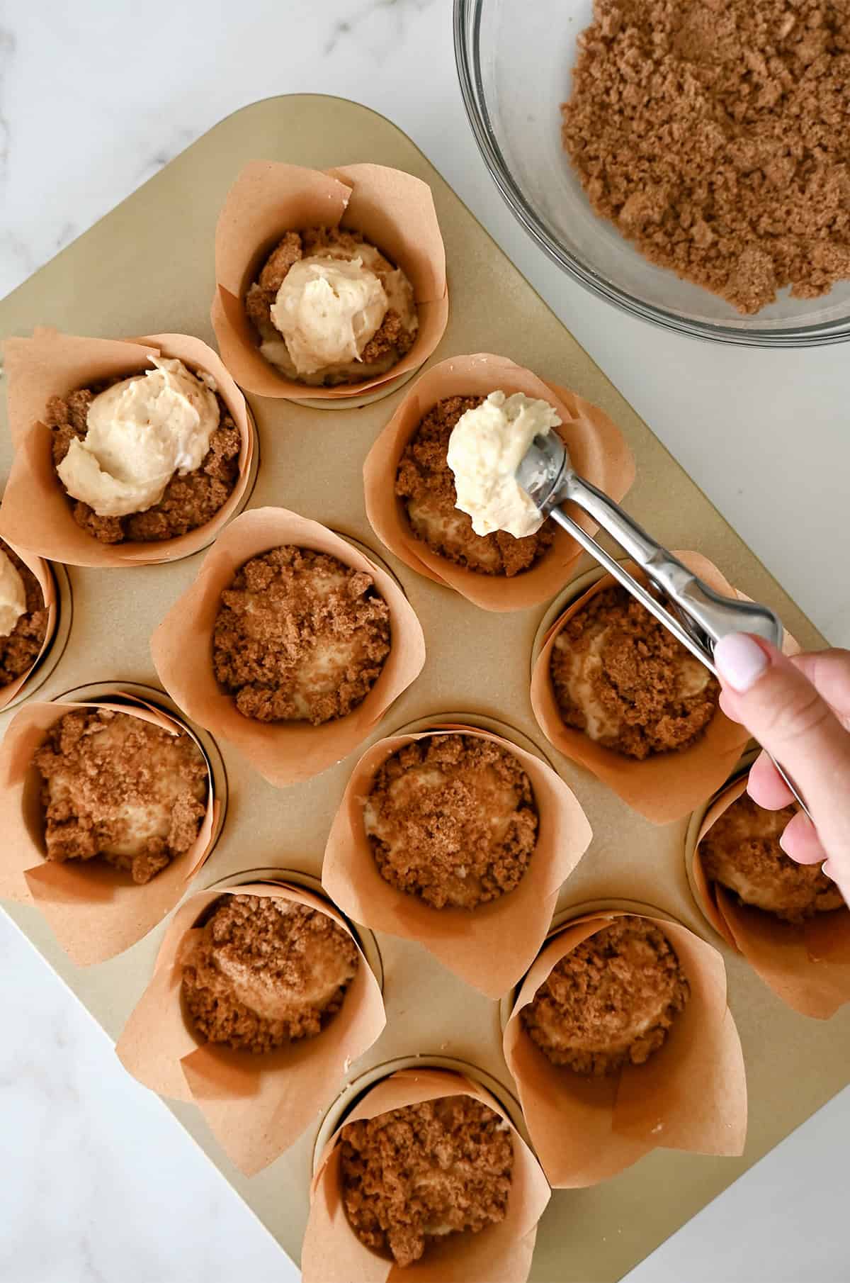 Layering coffee cake batter atop cinnamon streusel in a lined muffin pan.