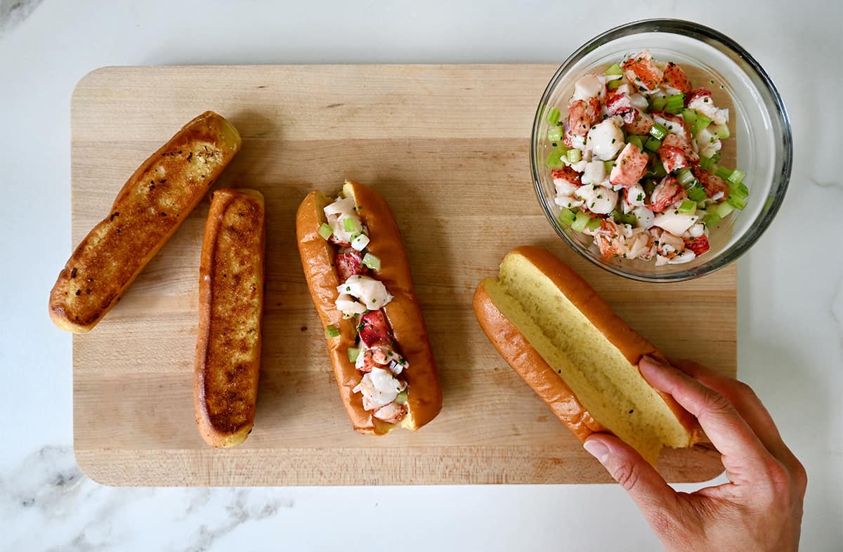 Split-top buns on a cutting board being filled with lobster salad.