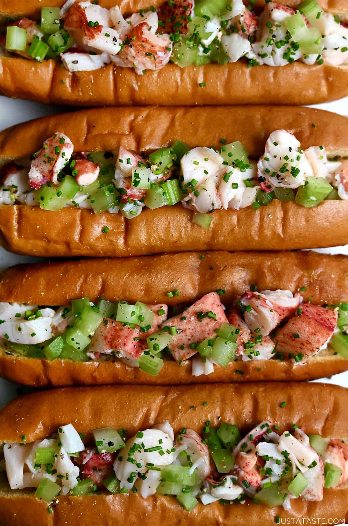 Split-top buns filled with lobster salad and garnished with black pepper and fresh chives.