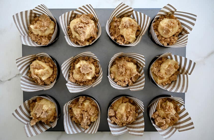 A top-down view of unbaked muffins topped with streusel in a lined muffin tin