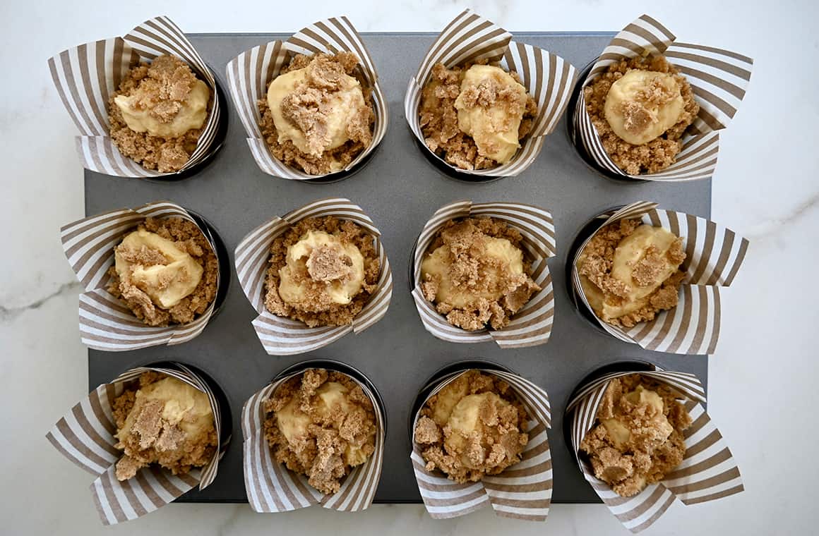 A top-down view of unbaked muffins topped with streusel in a lined muffin tin.