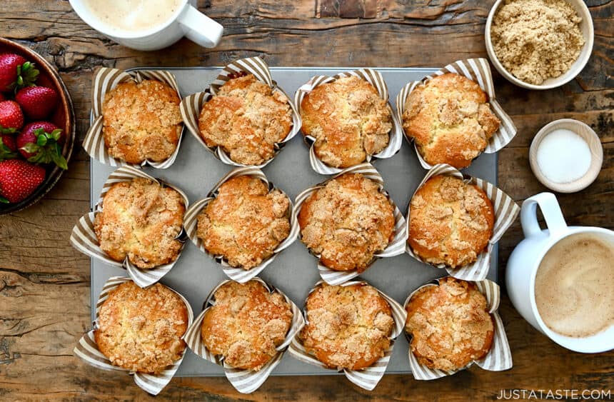 Sour Cream Coffee Cake Muffins in a muffin tin next to two mugs with whole milk lattes