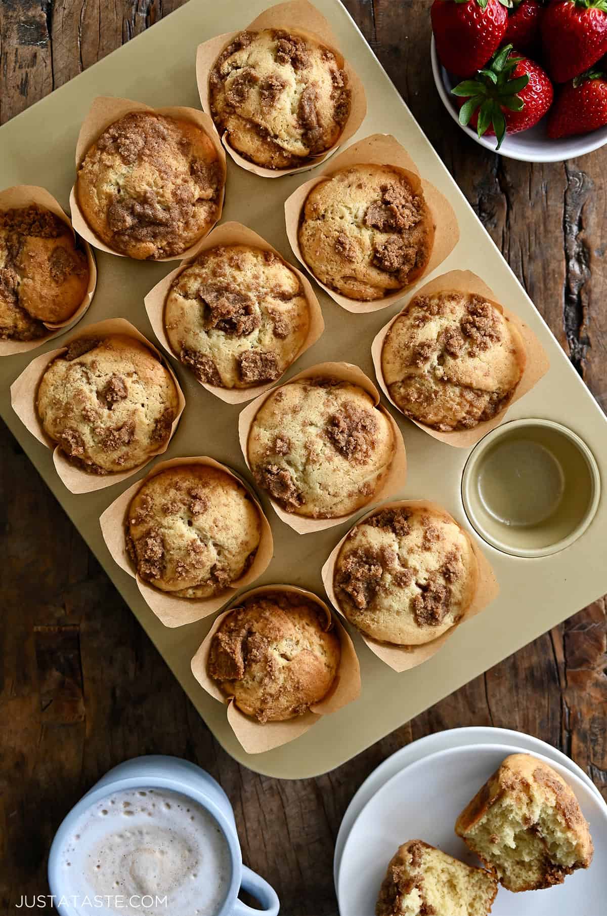Coffee cake muffins with cinnamon streusel in a muffin pan, with one on a plate, sliced open and slathered with butter.