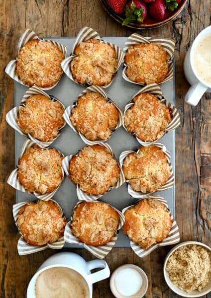 A top-down view of Sour Cream Coffee Cake Muffins with Streusel in a muffin tin next to a latte