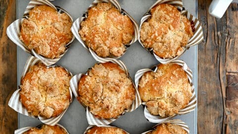 A top-down view of Sour Cream Coffee Cake Muffins with Streusel in a muffin tin next to a latte