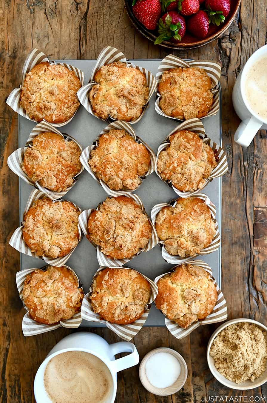 A top-down view of Sour Cream Coffee Cake Muffins with Streusel in a muffin tin next to a latte