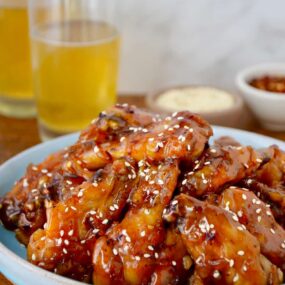 Crispy Baked Orange Chicken Wings on pale blue plate with two glasses of beer in background.