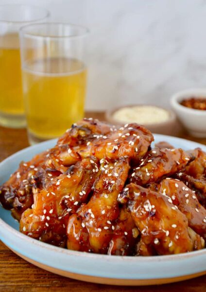 Crispy Baked Orange Chicken Wings on pale blue plate with two glasses of beer in background.