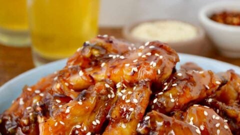 Crispy Baked Orange Chicken Wings on pale blue plate with two glasses of beer in background.