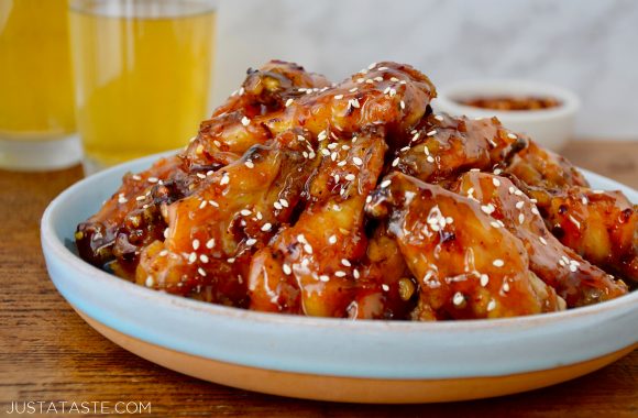 Crispy Baked Orange Chicken Wings on pale blue plate garnished with sesame seeds; two glasses of beer and small ramekin with red pepper flakes in background.