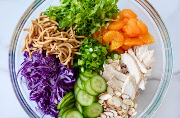 A large glass bowl containing chopped lettuce, cucumbers, scallions and chicken