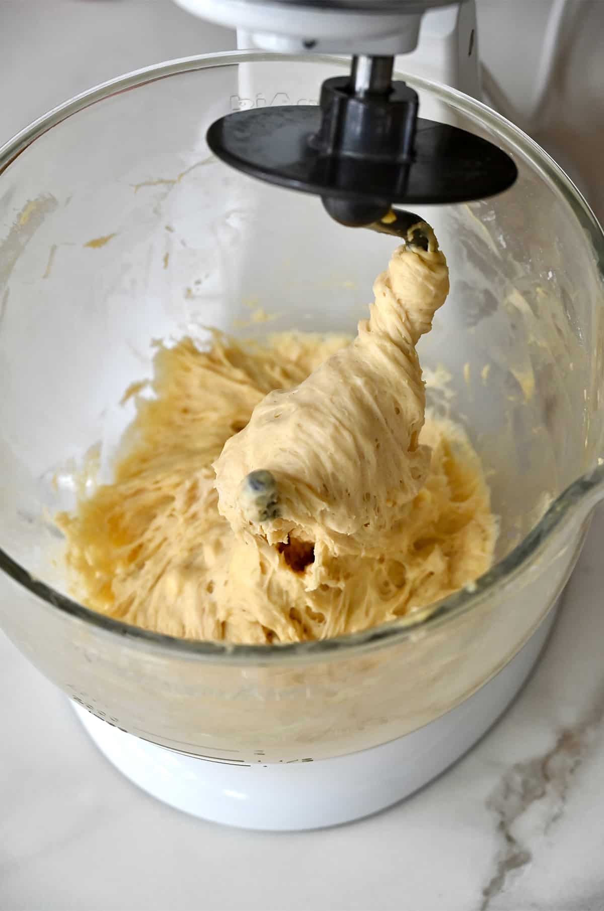 A stand mixer with the dough hook covered with pizza dough.