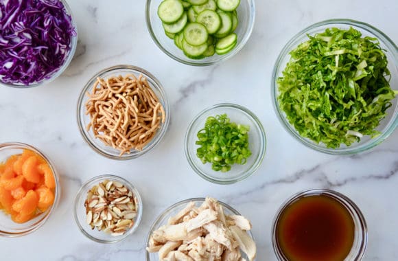 Small glass bowls containing lettuce, red cabbage, chicken, scallions and almonds