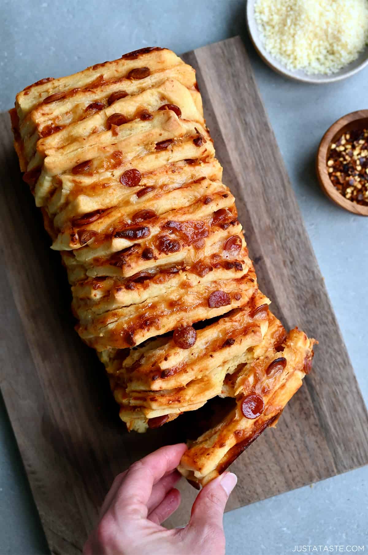 A hand reaches for a pepperoni pull-apart pizza bread on a wood cutting board. 