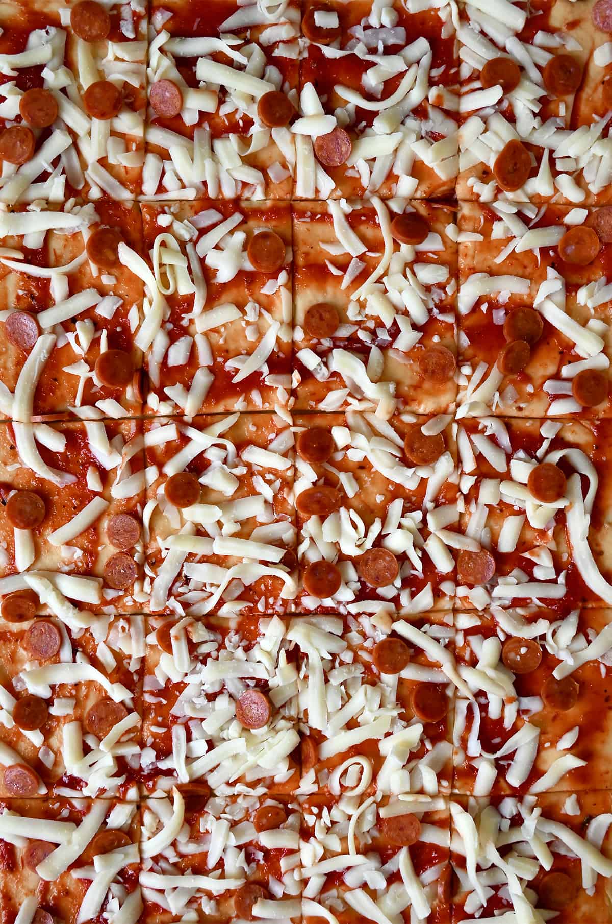 Pizza dough topped with marinara sauce, shredded cheese and mini pepperoni sliced into uniform pieces.