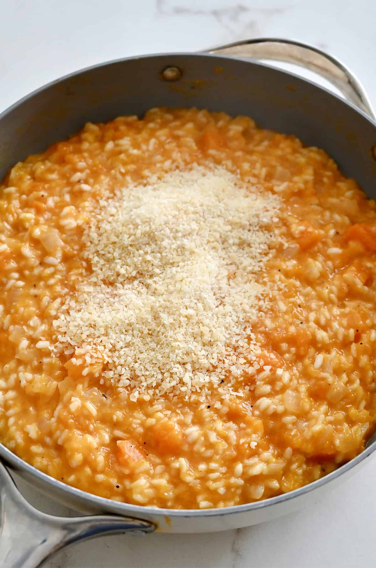 Grated Parmesan cheese being added to the creamy butternut squash risotto in a large skillet, just before stirring to finish the dish.