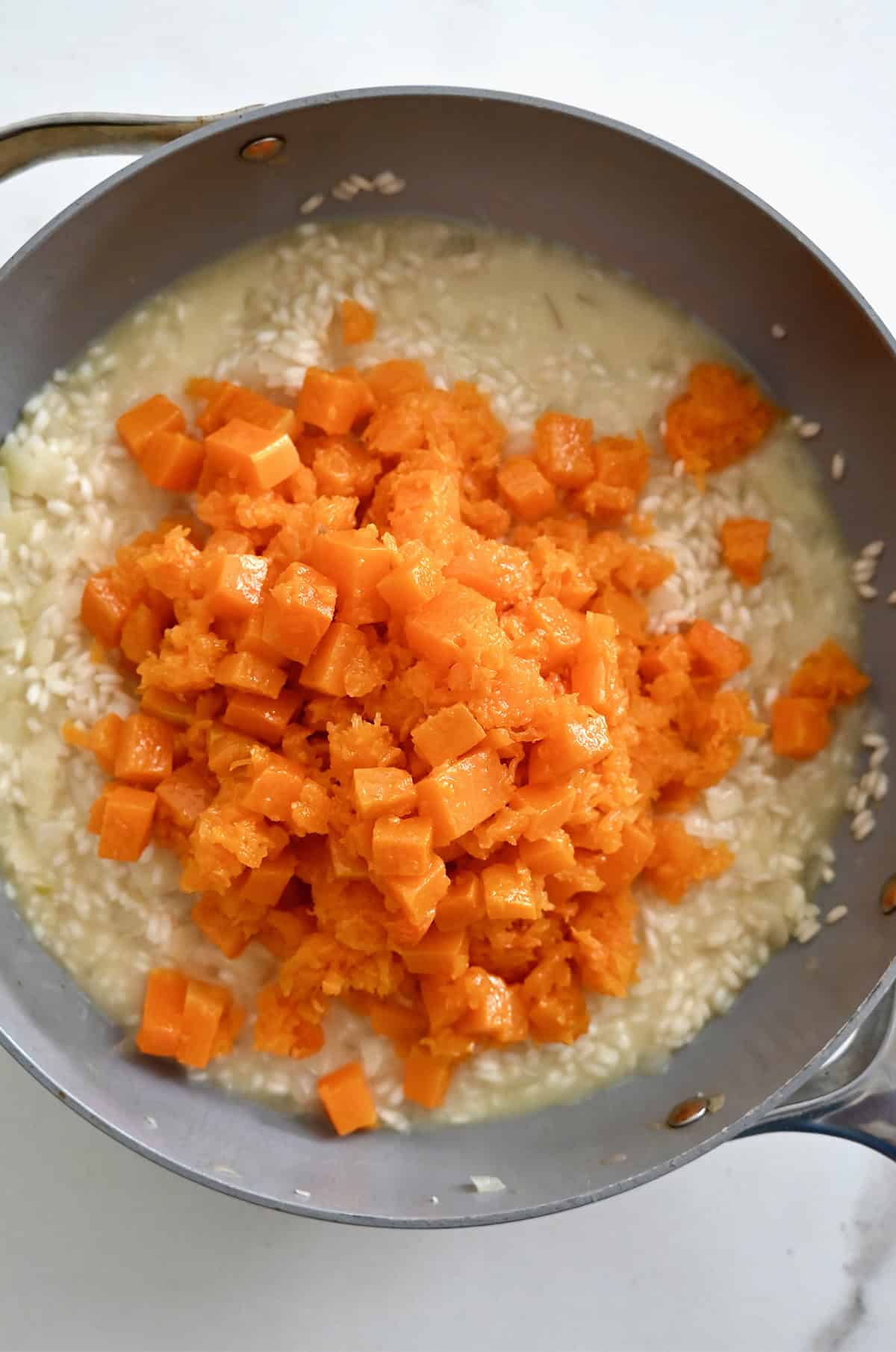 Roasted butternut squash being added to a saucepan with risotto.