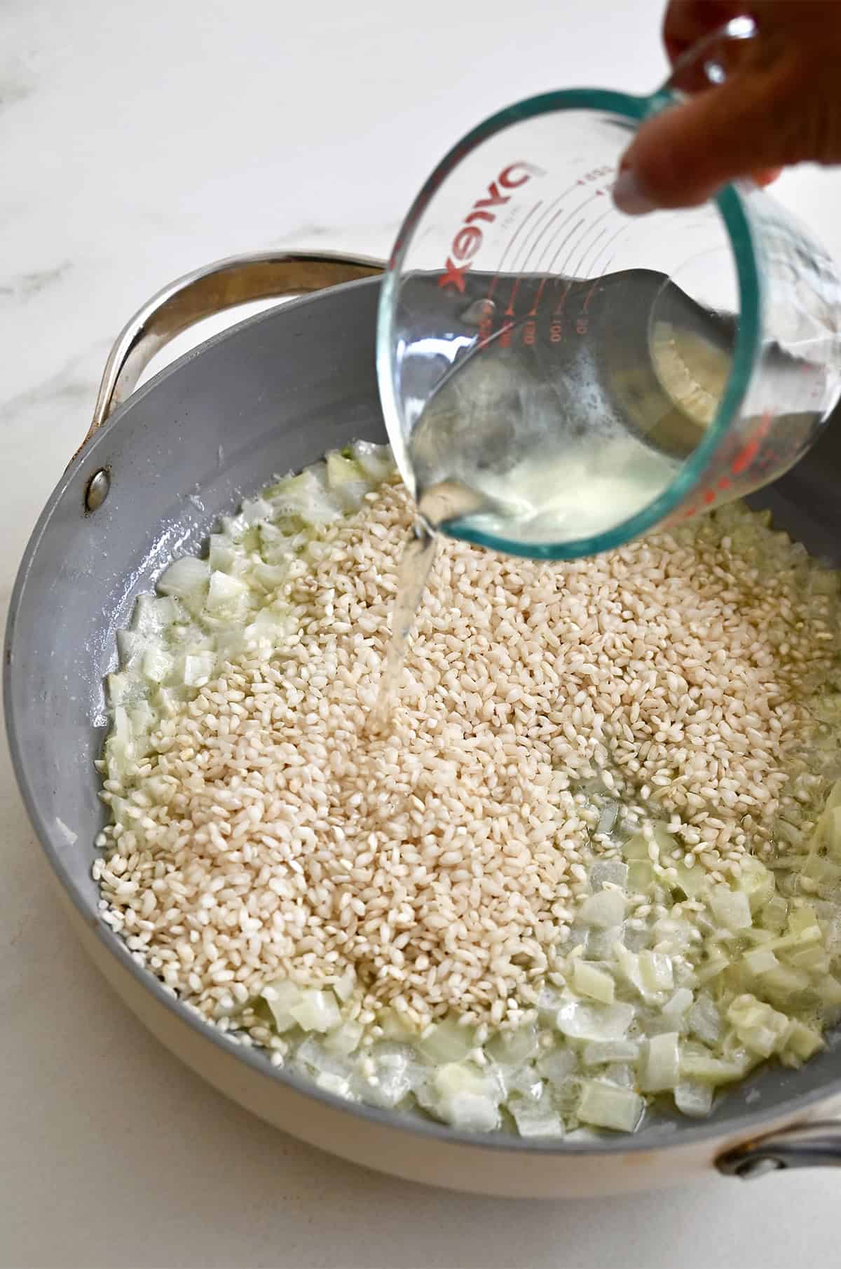 Adding dry white wine to a saucepan with Arborio rice and sautéed aromatics.