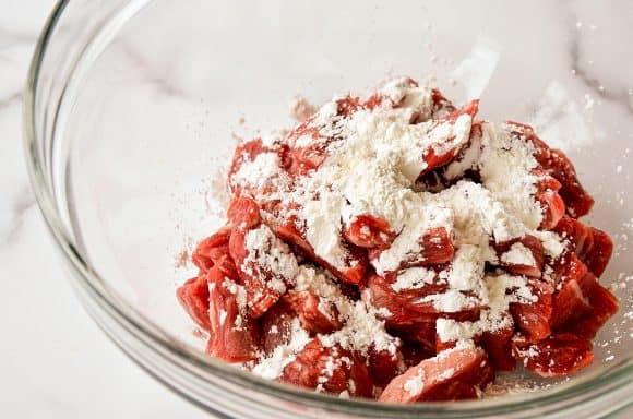 Clear bowl containing sliced flank steak covered in cornstarch