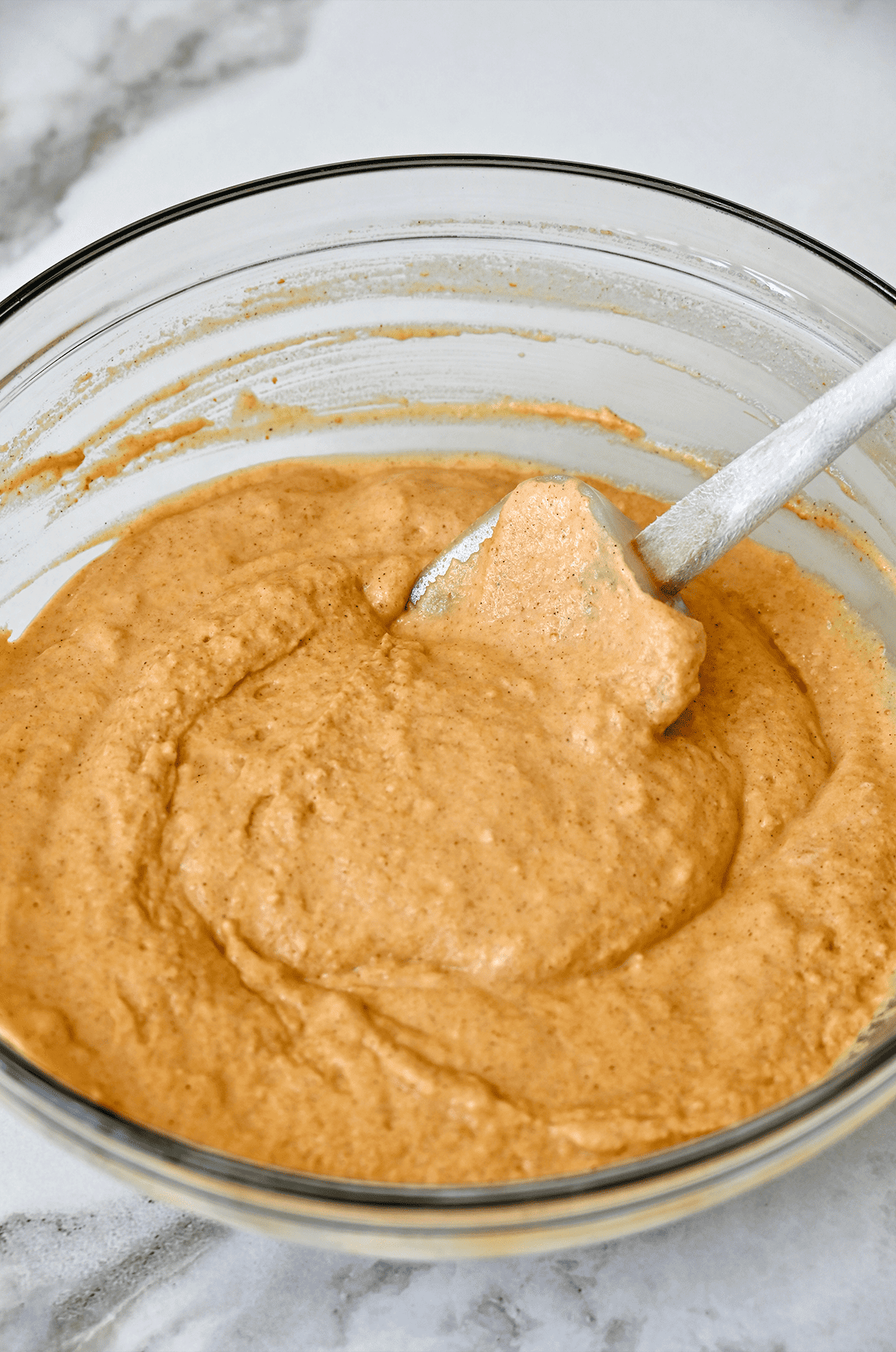 Pumpkin pancake batter in a clear bowl with a spatula.