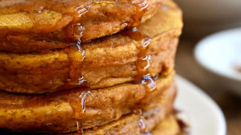 A tall stack of pumpkin pie pancakes topped with pecans, whipped cream and maple syrup.