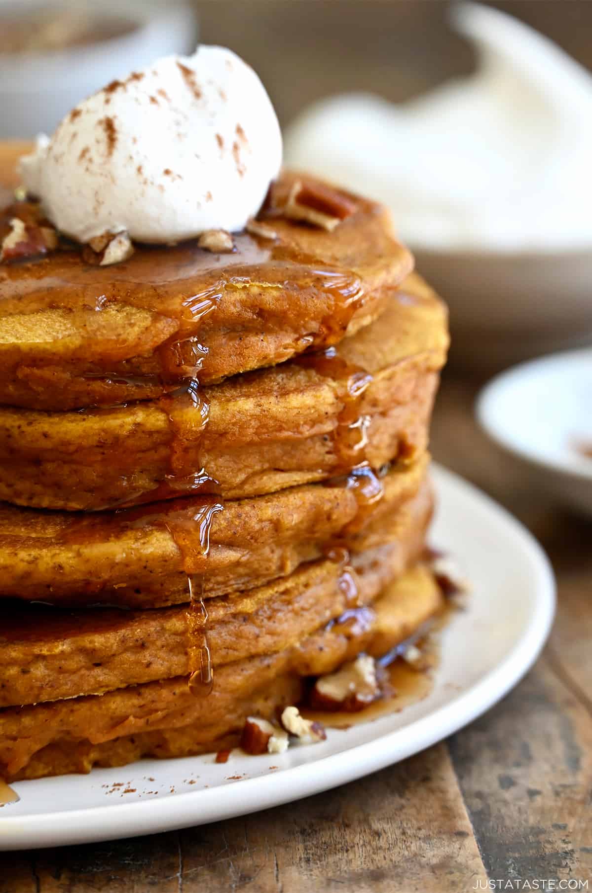 A tall stack of pumpkin pie pancakes topped with pecans, whipped cream and maple syrup.