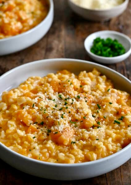 Butternut squash risotto topped with grated Parmesan cheese and chopped fresh chives in a bowl.