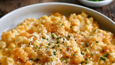 Butternut squash risotto topped with grated Parmesan cheese and chopped fresh chives in a bowl.