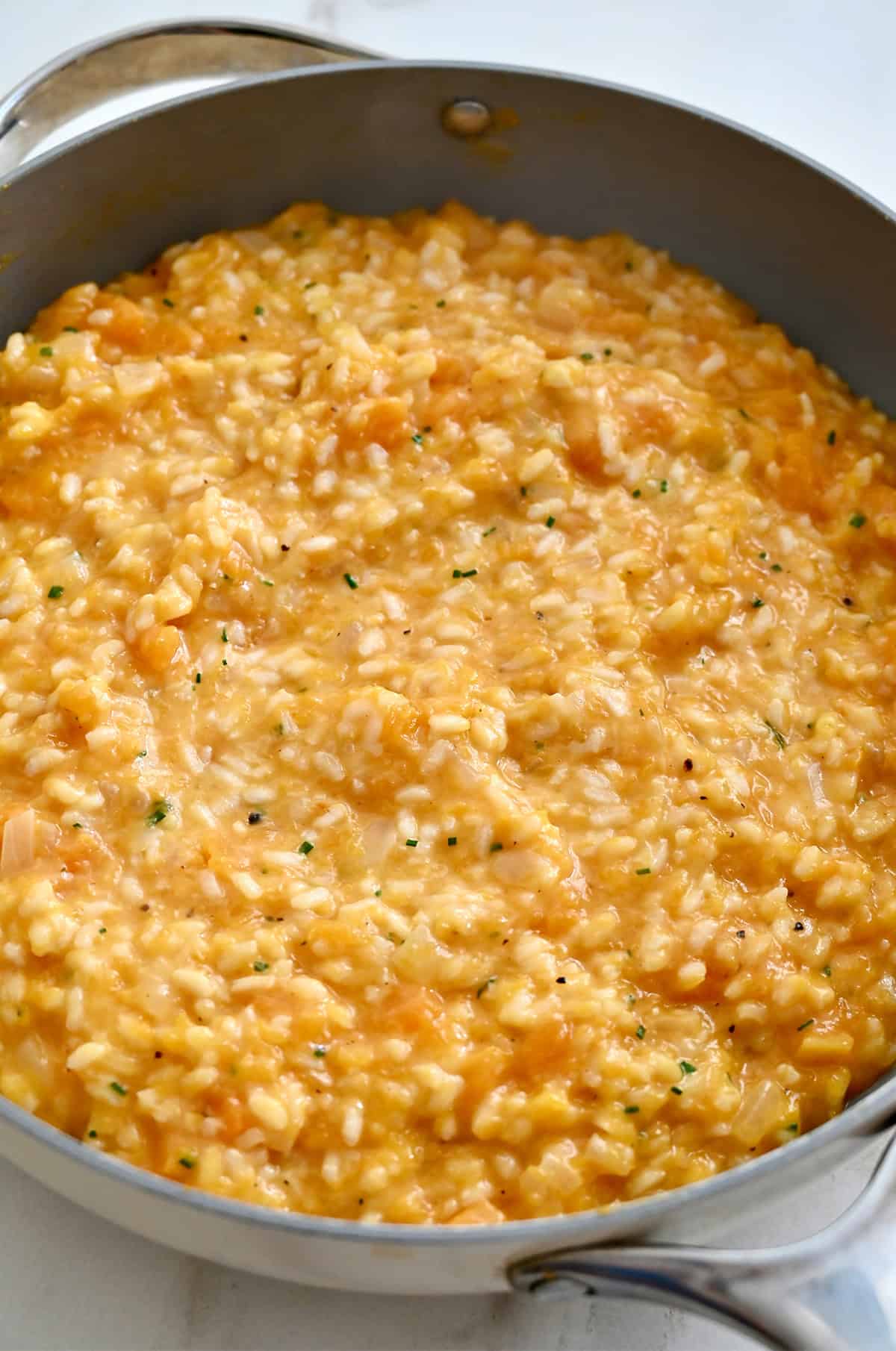 Finished butternut squash risotto in a large skillet, golden and creamy with flecks of fresh chives, ready to serve.