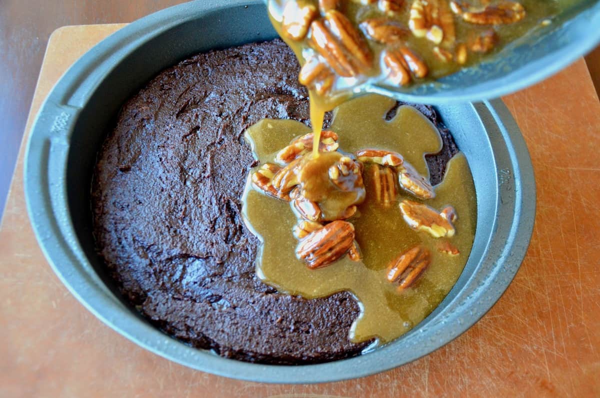 Pecan Pie Topping is being poured over a round cake pan of cooked brownies.