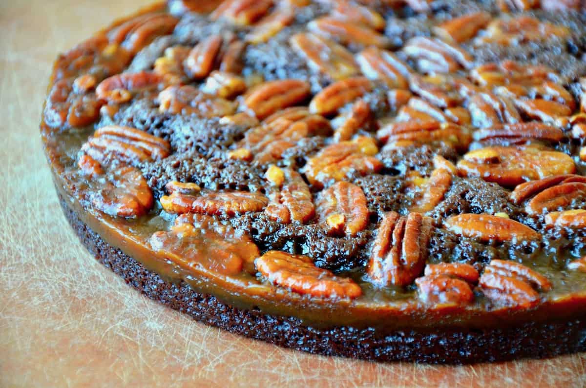 An uncut cake of pecan pie brownies sits on a cutting board.