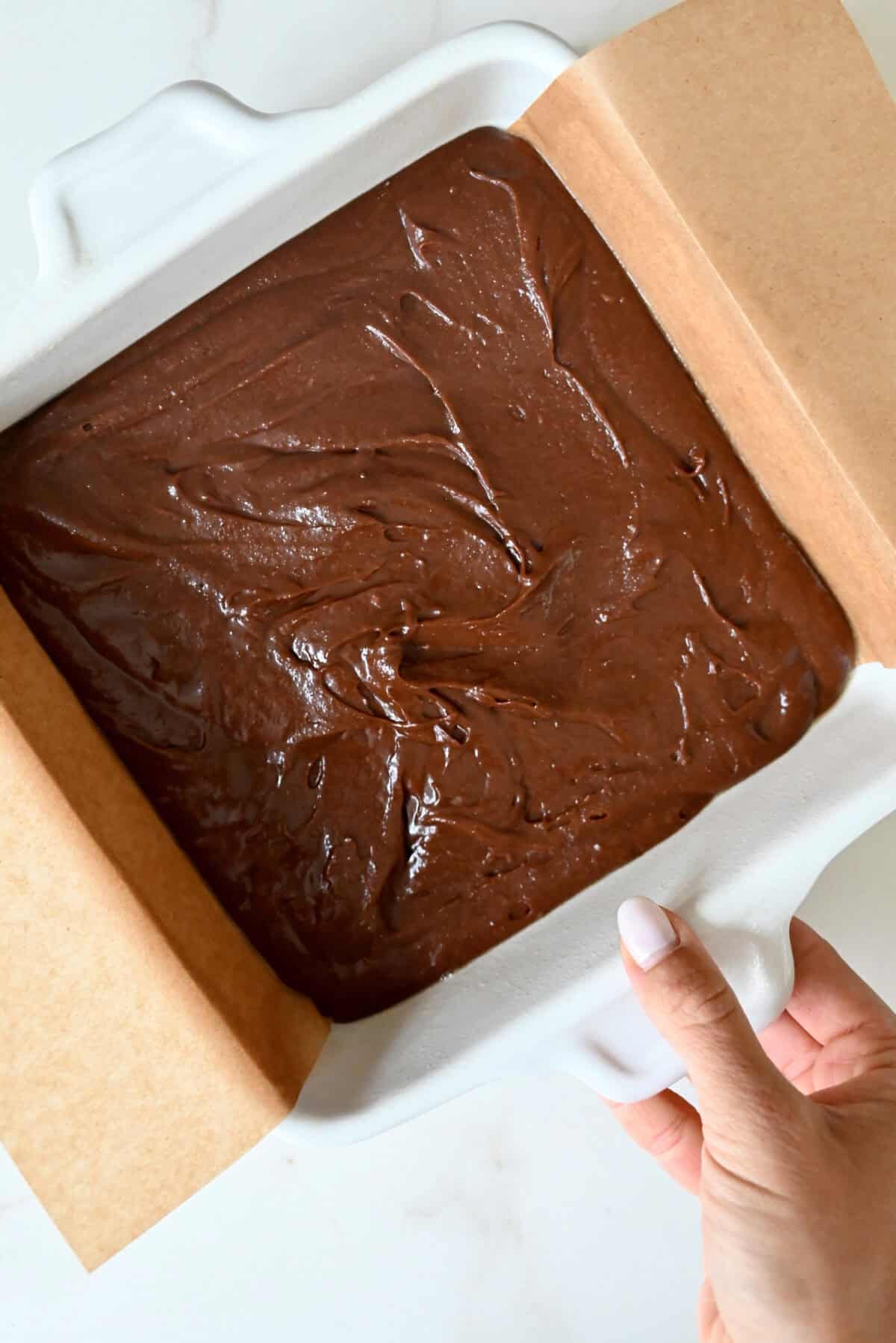 Brownie batter in a parchment paper-lined 8-inch baking pan.