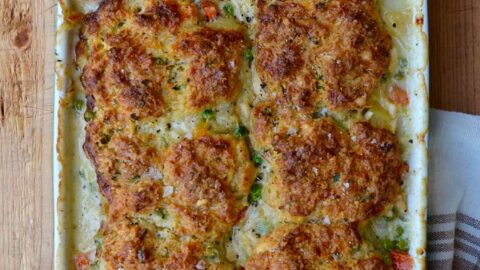 A white baking dish with turkey pot pie and biscuits and small bowls of herbs and salt