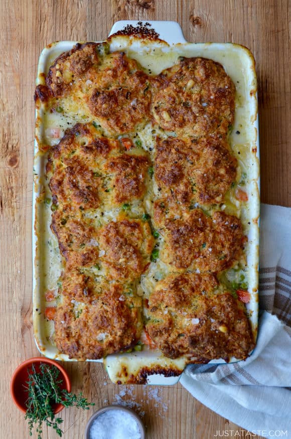 A white baking dish with turkey pot pie and biscuits and small bowls of herbs and salt