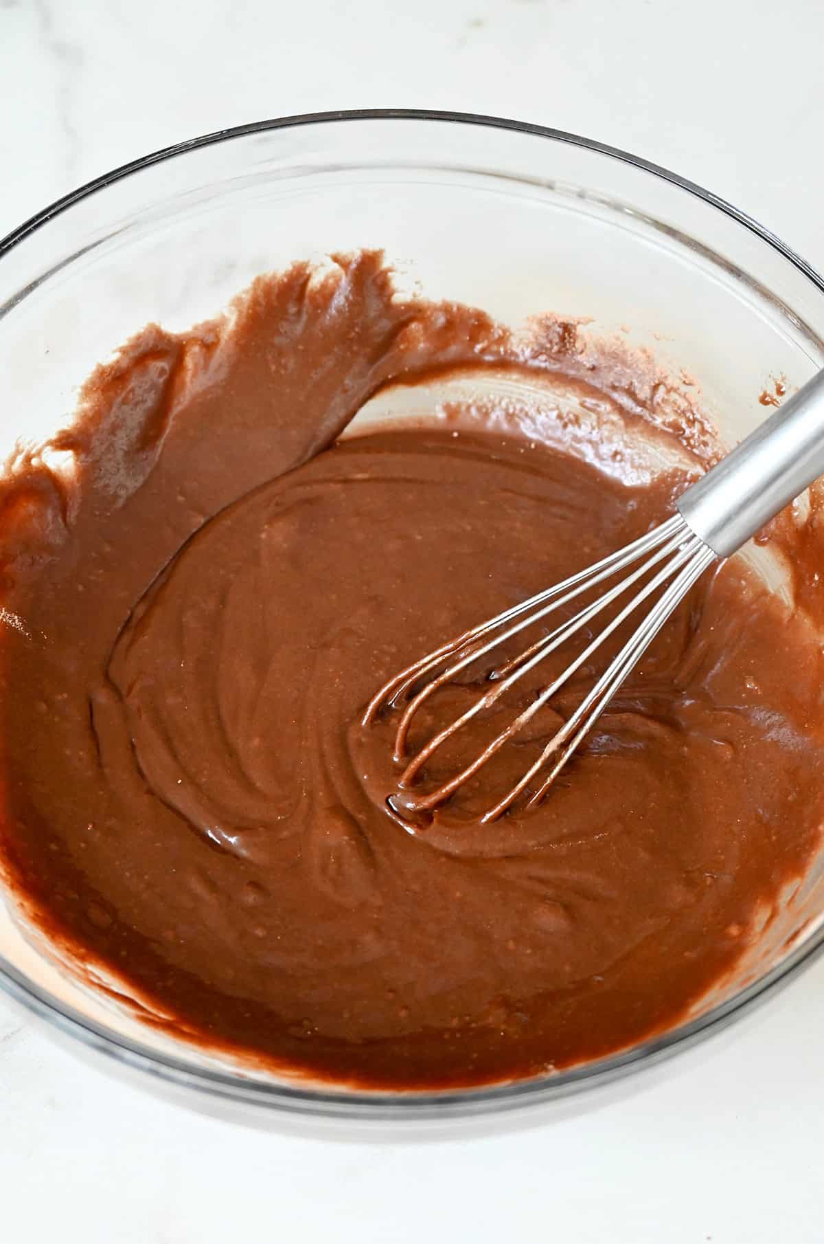 Brownie batter in a glass bowl with a whisk.