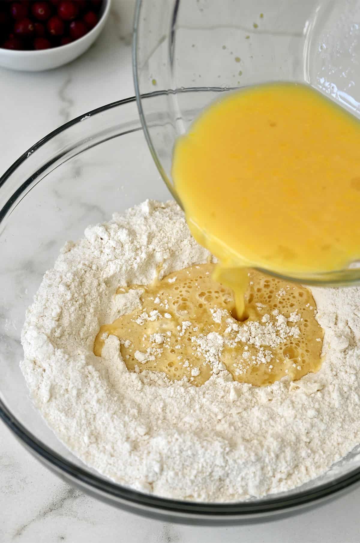 Orange juice being poured into a bowl with flour.