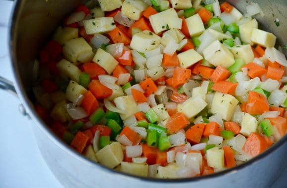 A stockpot filled with chopped vegetables and herbs